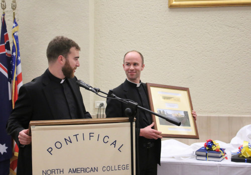 Grayson Heenan ('17) and Rev. Mr. James Morin ('16) present a gift to Msgr. Checchio.